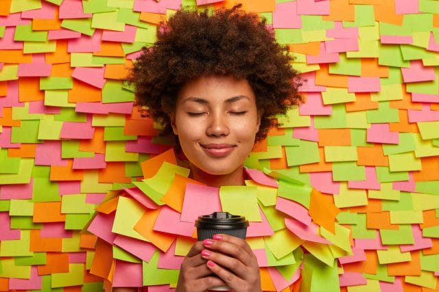 Calm relaxed woman drinks coffee on bed of post it notes.