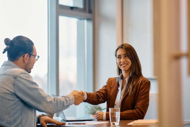 Business Woman shaking gentleman's hand sitting at a desk.